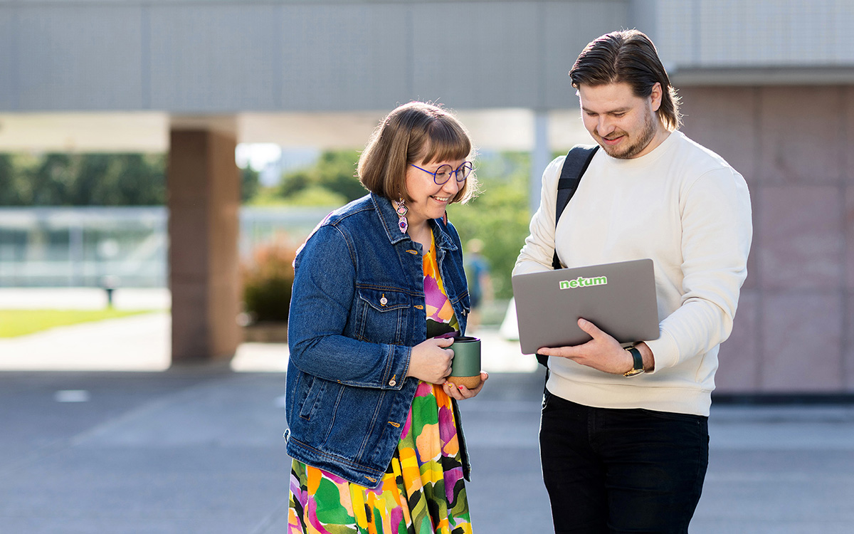 Kaksi henkilöä katsoo avoinaisen kannettavan tietokoneen näyttöä rakennuksen pihalla.