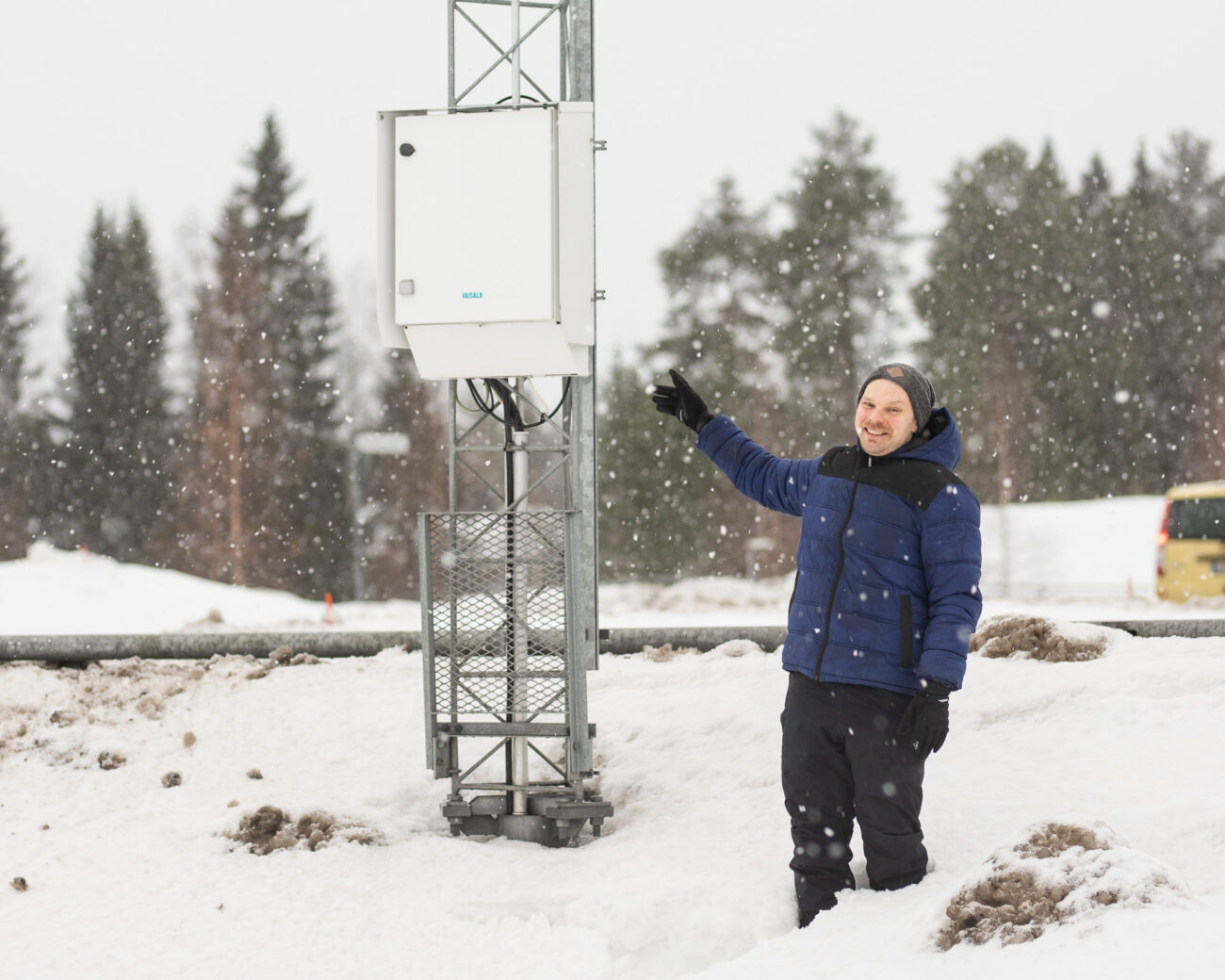A senior embedded systems developer pointing at a Vaisala weather station unit in freezing conditions.