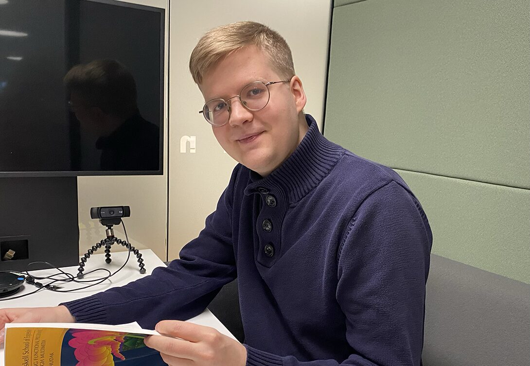 Iloinen sulautettujen järjestelmien kehittäjä katsoo kameraan ja selaa samalla kirjaa.