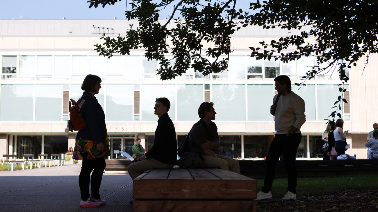 Neljä ihmistä Turun yliopiston edustalla varjossa puun alla. Kaksi heistä seisoo, kaksi istuu.