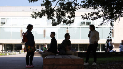 Neljä ihmistä Turun yliopiston edustalla varjossa puun alla. Kaksi heistä seisoo, kaksi istuu.